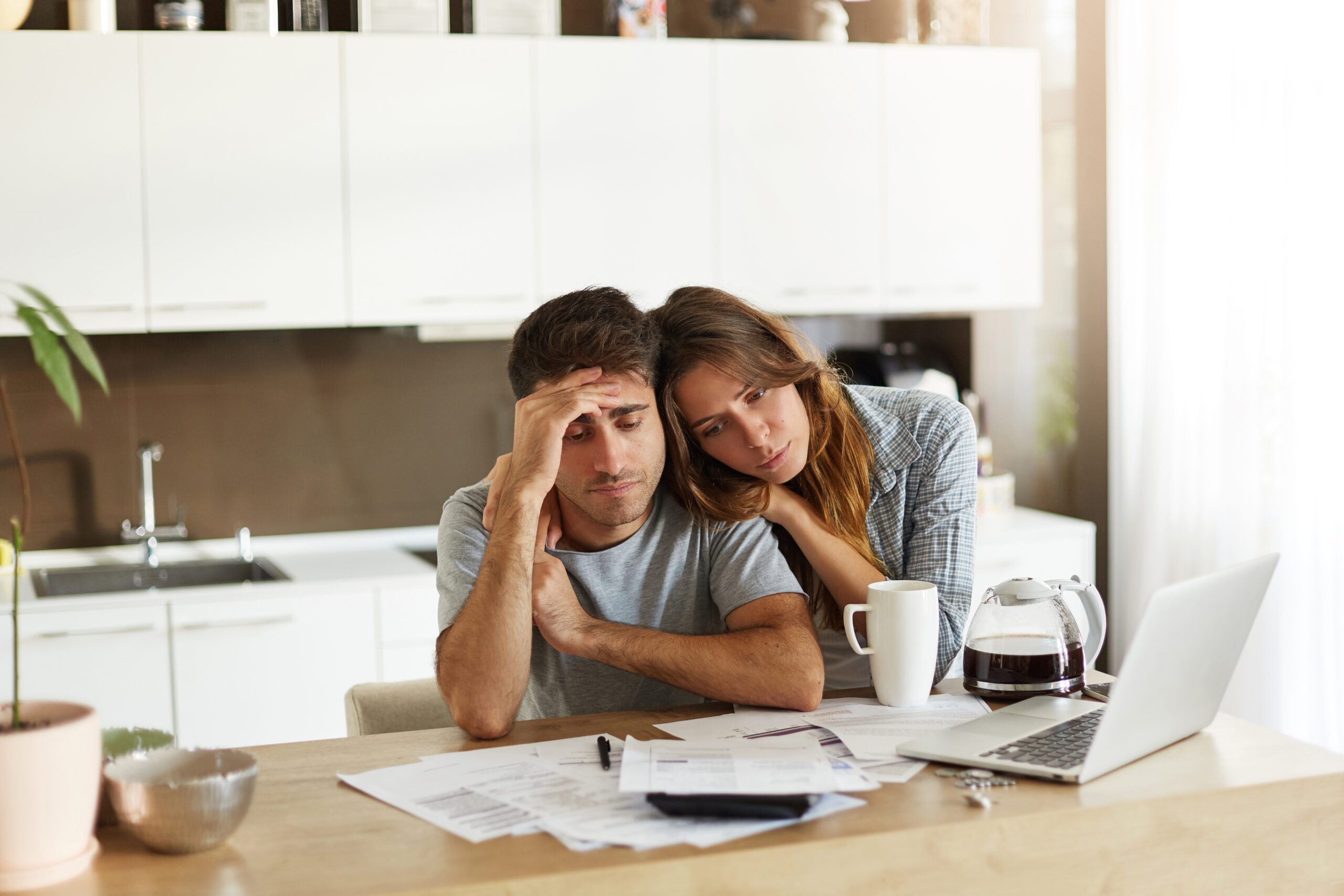 Stressed wife and husband with many debts doing paperwork together, reviewing their expenses, planning domestic budget and calculating bills in kitchen, surrounded with papers, calculator and laptop 10113435-young-couple-checking-their-family-budget
