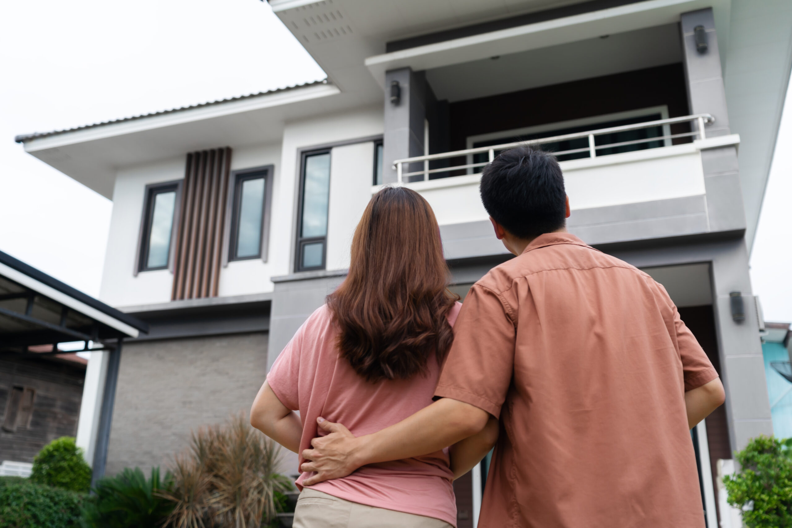 couple standing outside and looking their house young-couple-standing-outside-looking-their-house