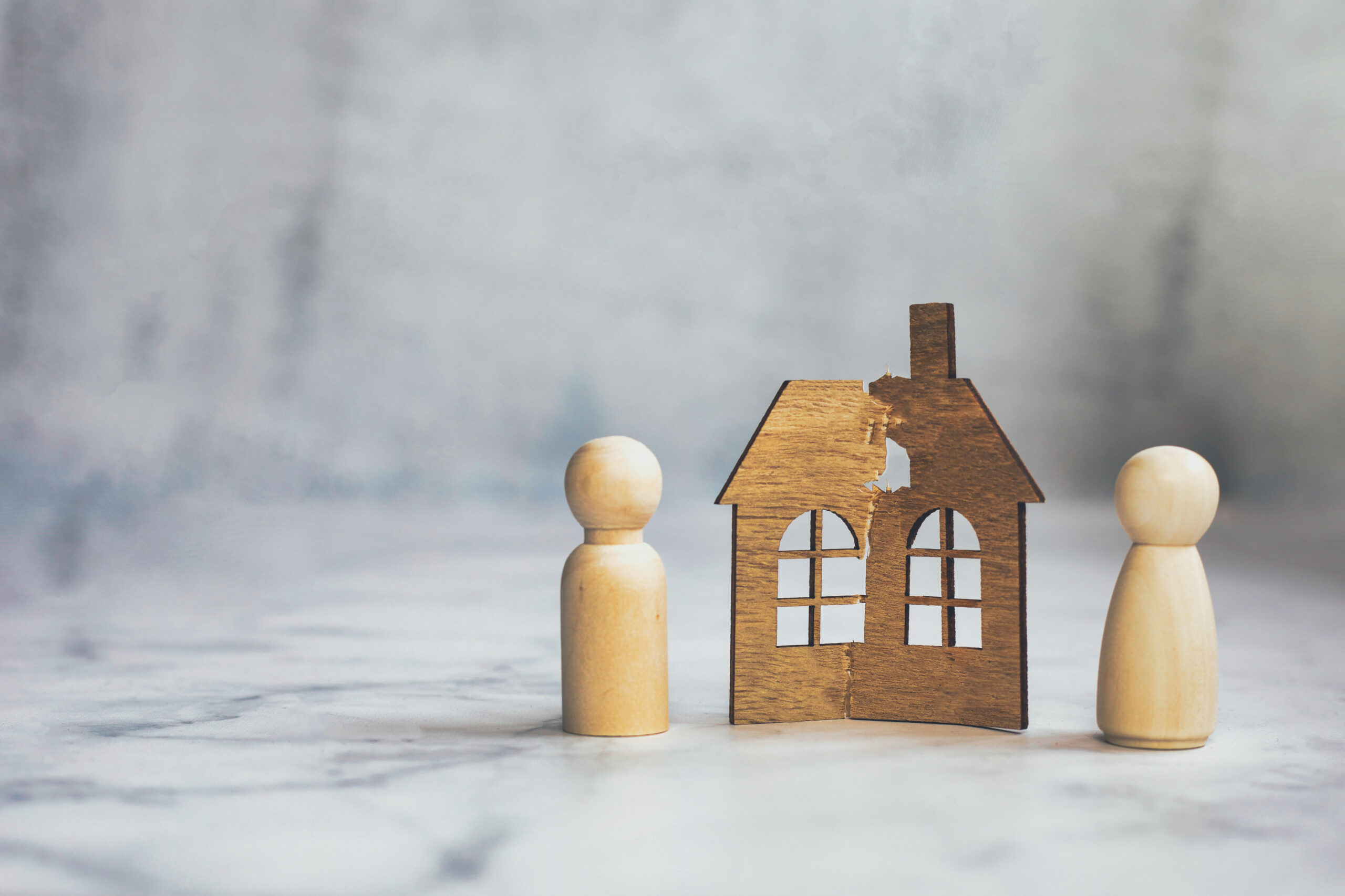 Divorce, division of property, poverty and no money concept. Wooden broken house on light background. Mortgage, rent, realtor concept copy space space for text two wooden figures with a wooden house