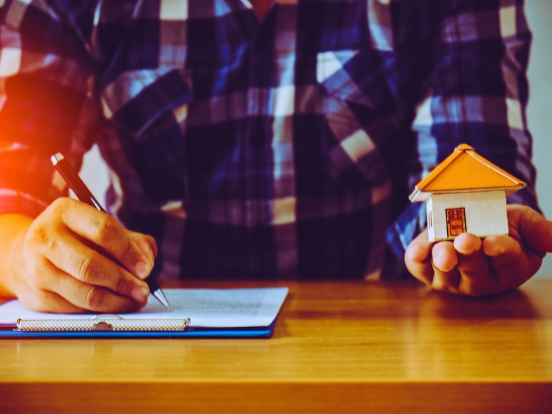 Blog 6 Man signing document while holding a small toy house model.